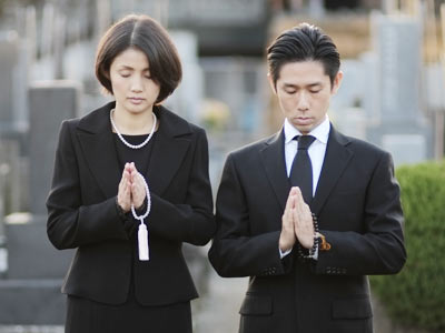墓前で手を合わせる夫婦の写真